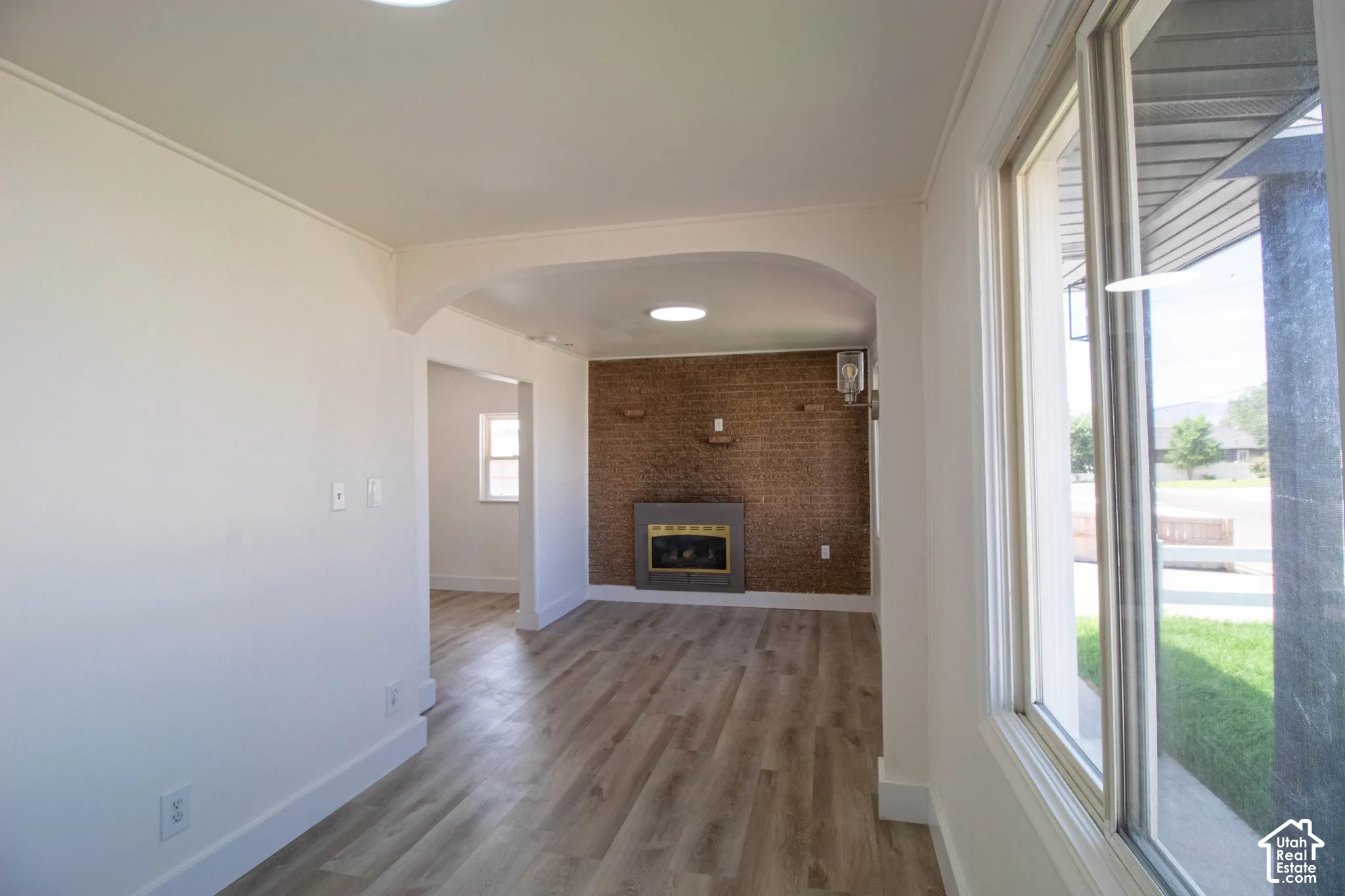 Bright interior featuring wood-finish flooring, an arched doorway, and a brick accent wall with a built-in fireplace