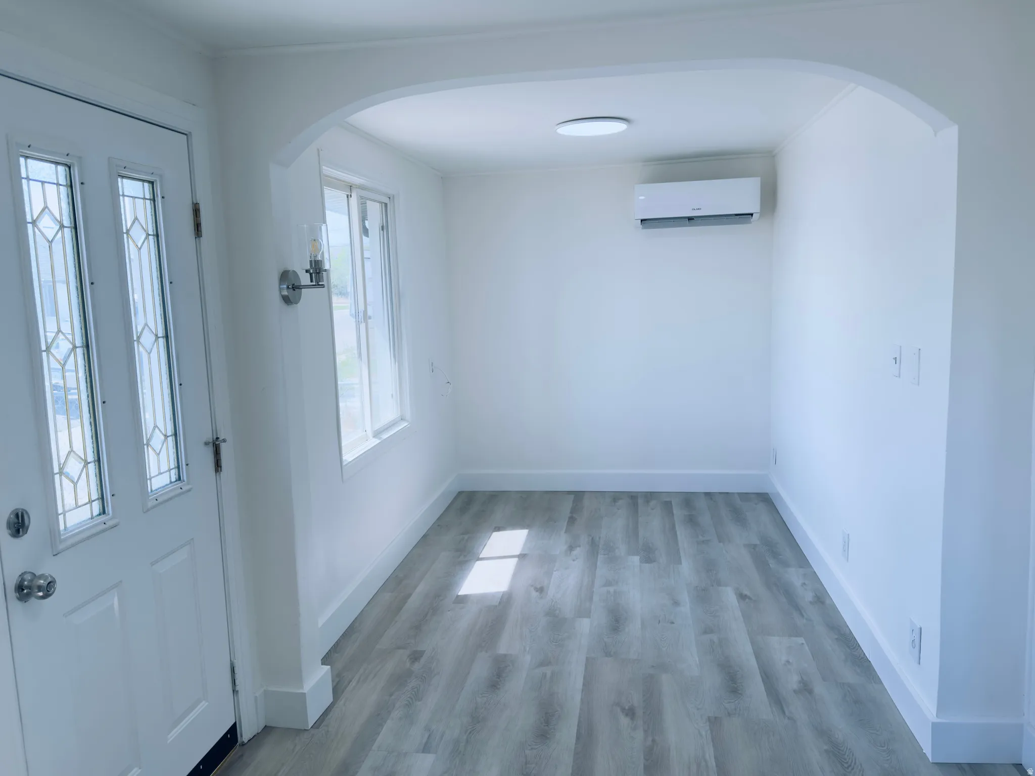 Entryway featuring a decorative glass panel door, wood-finish flooring, an arched doorway, and a wall-mounted mini-split system