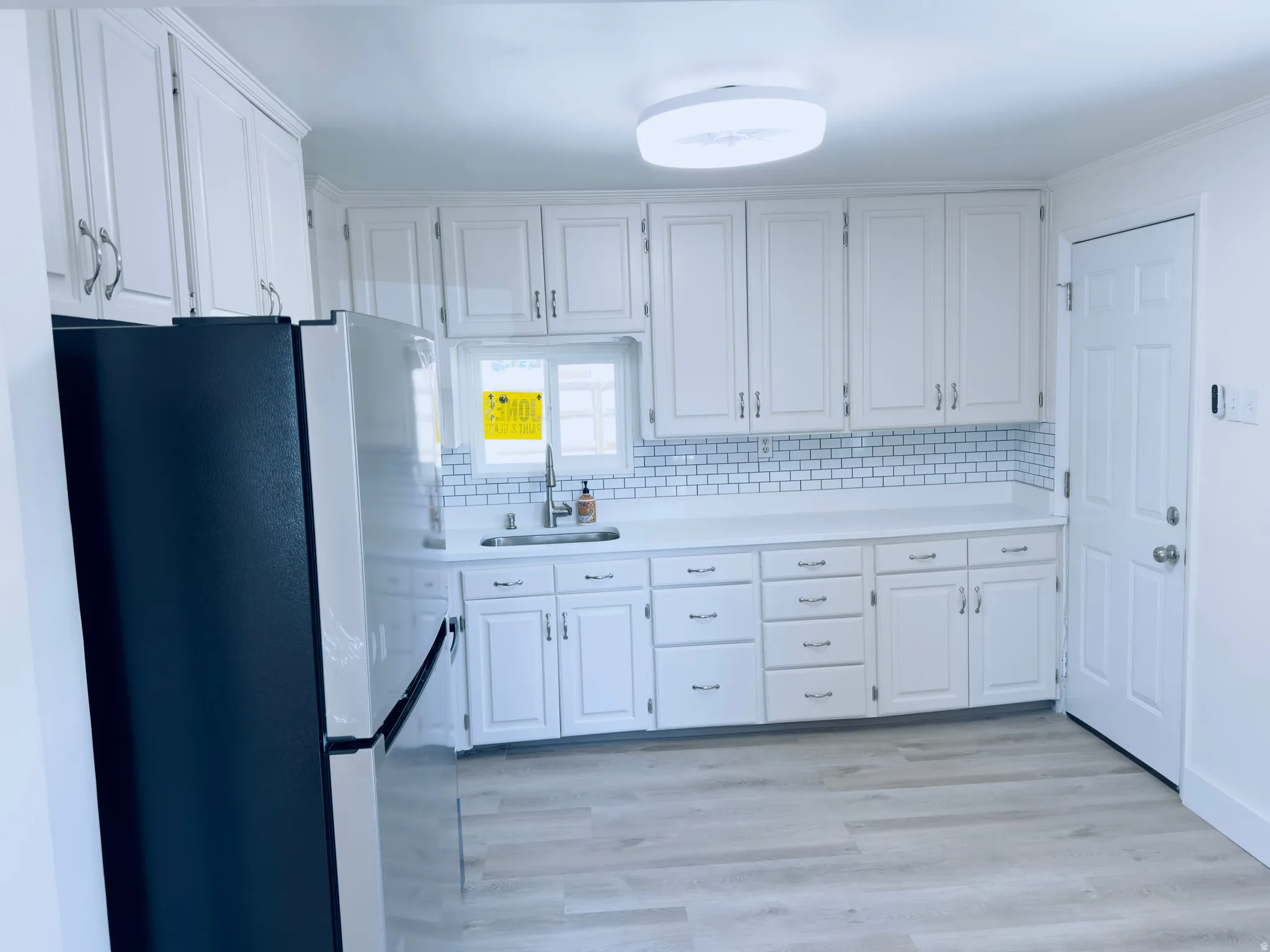 Bright kitchen featuring white shaker cabinetry, subway tile backsplash, light wood-finish flooring, and a stainless steel sink with a gooseneck faucet
