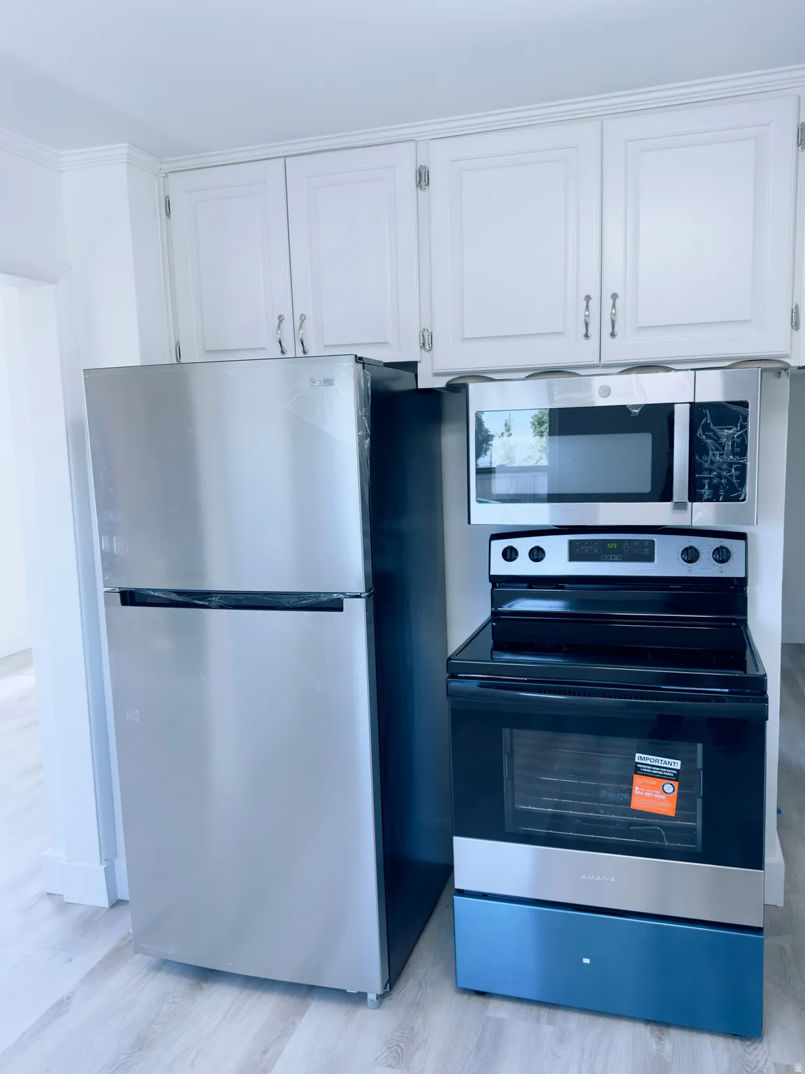 Kitchen featuring new stainless steel appliances, white upper cabinetry with chrome hardware, and wood-finish flooring
