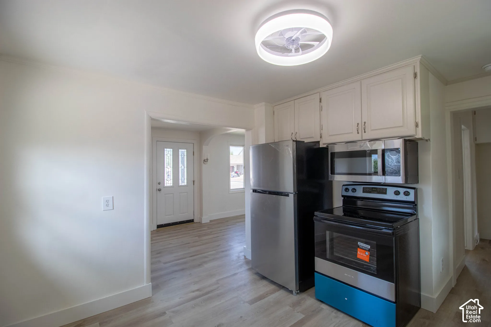 Kitchen featuring light wood-finish flooring, white cabinetry, stainless steel refrigerator, stainless steel microwave, and electric range