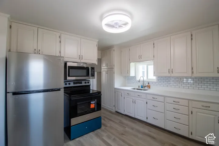 Bright kitchen featuring white cabinetry, subway tile backsplash, light countertops, wood-finish flooring, and a stainless steel appliance suite