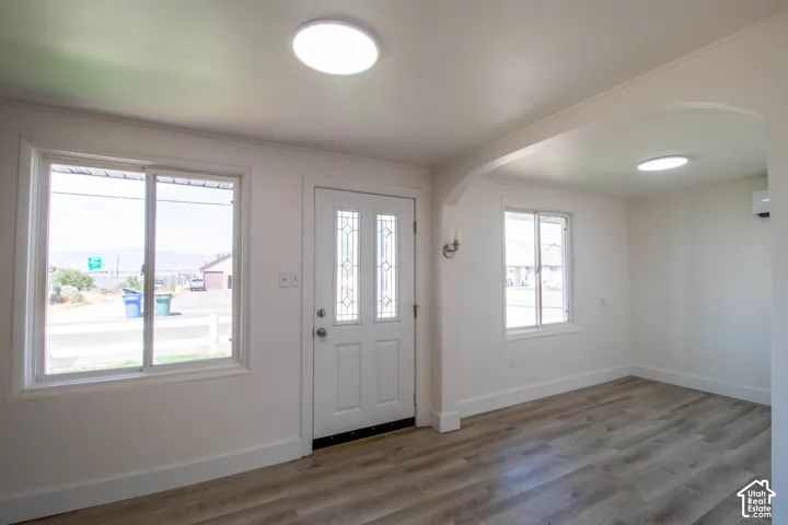 Entryway featuring a decorative glass front door, two large windows, wood-finish flooring, a wall sconce, and an arched doorway