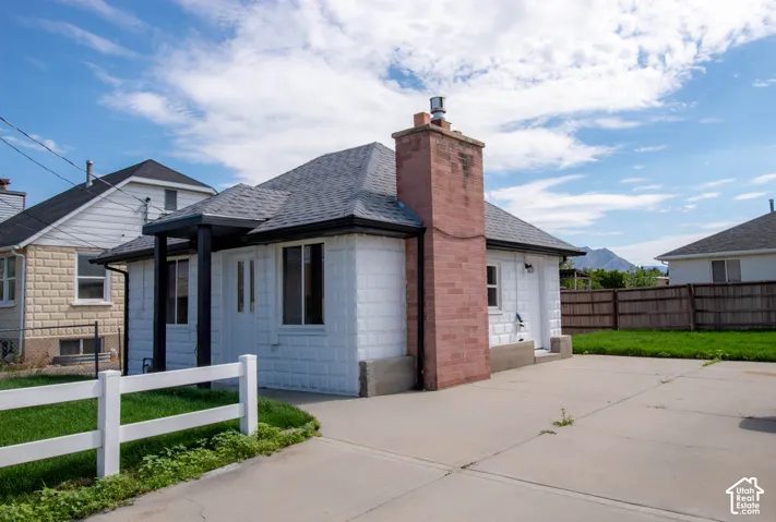 White exterior featuring a dark gray shingle roof, a prominent brick chimney, and a concrete driveway