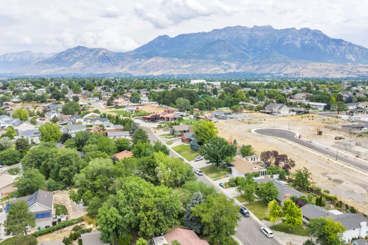 Expansive mountain backdrop with a residential area featuring mature trees, paved streets, and a new development area with a cul-de-sac