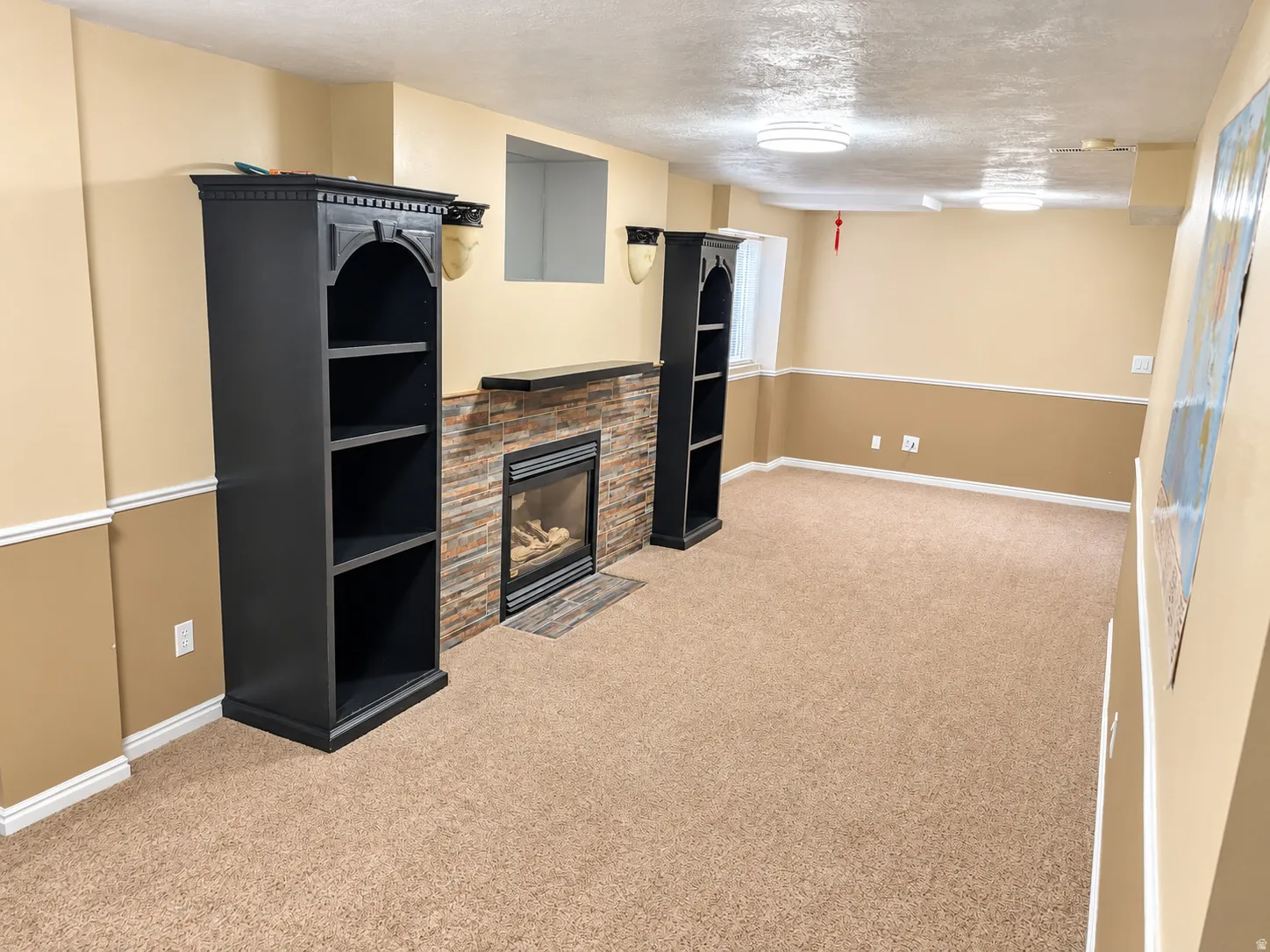 Recessed fireplace with stone surround, two built-in shelving units, textured ceiling, and carpeting