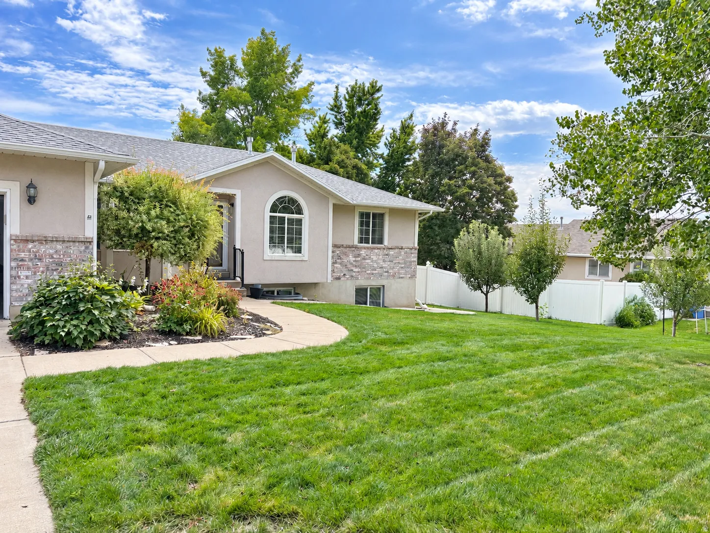 Stucco exterior with stone accents, arched window, attached garage, concrete pathway, and a landscaped front yard