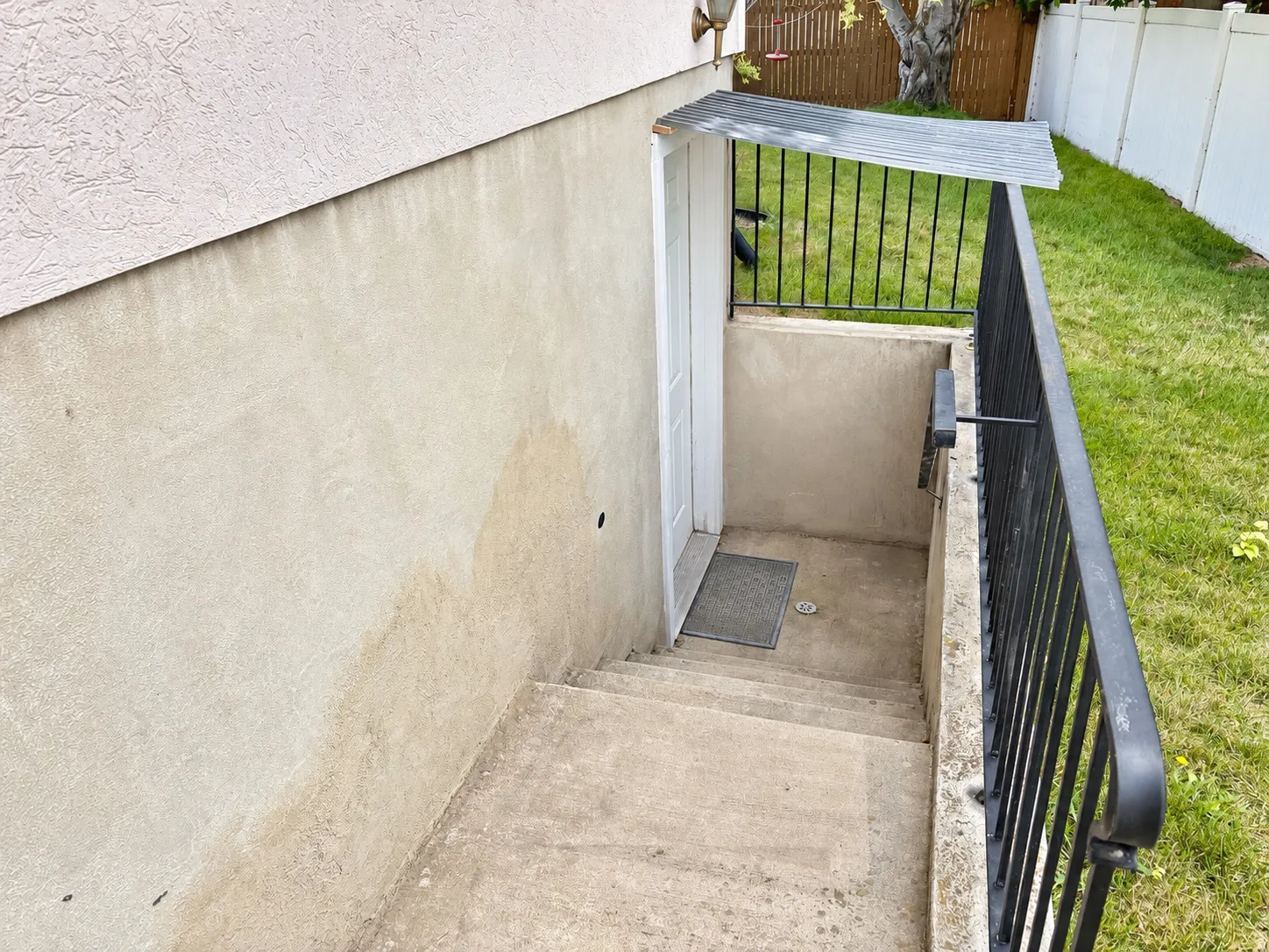 Exterior access featuring a corrugated metal awning, black metal handrails, and a white entry door