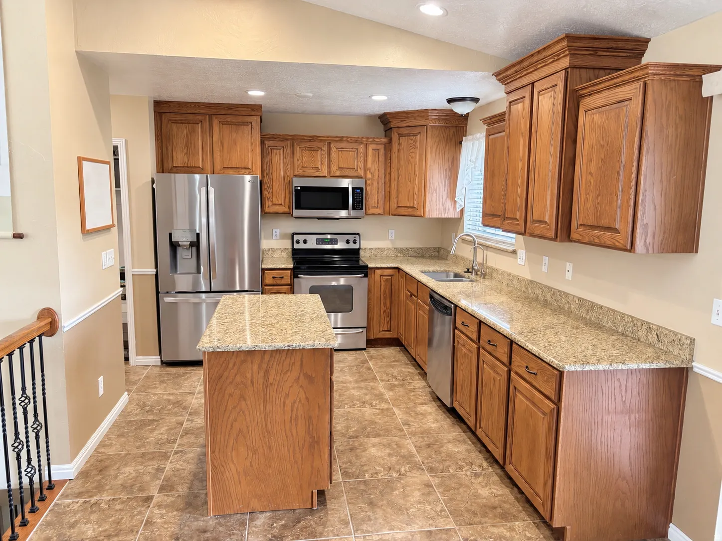 Kitchen featuring wood cabinetry, stainless steel appliances, a center island, granite-style countertops, and tile flooring