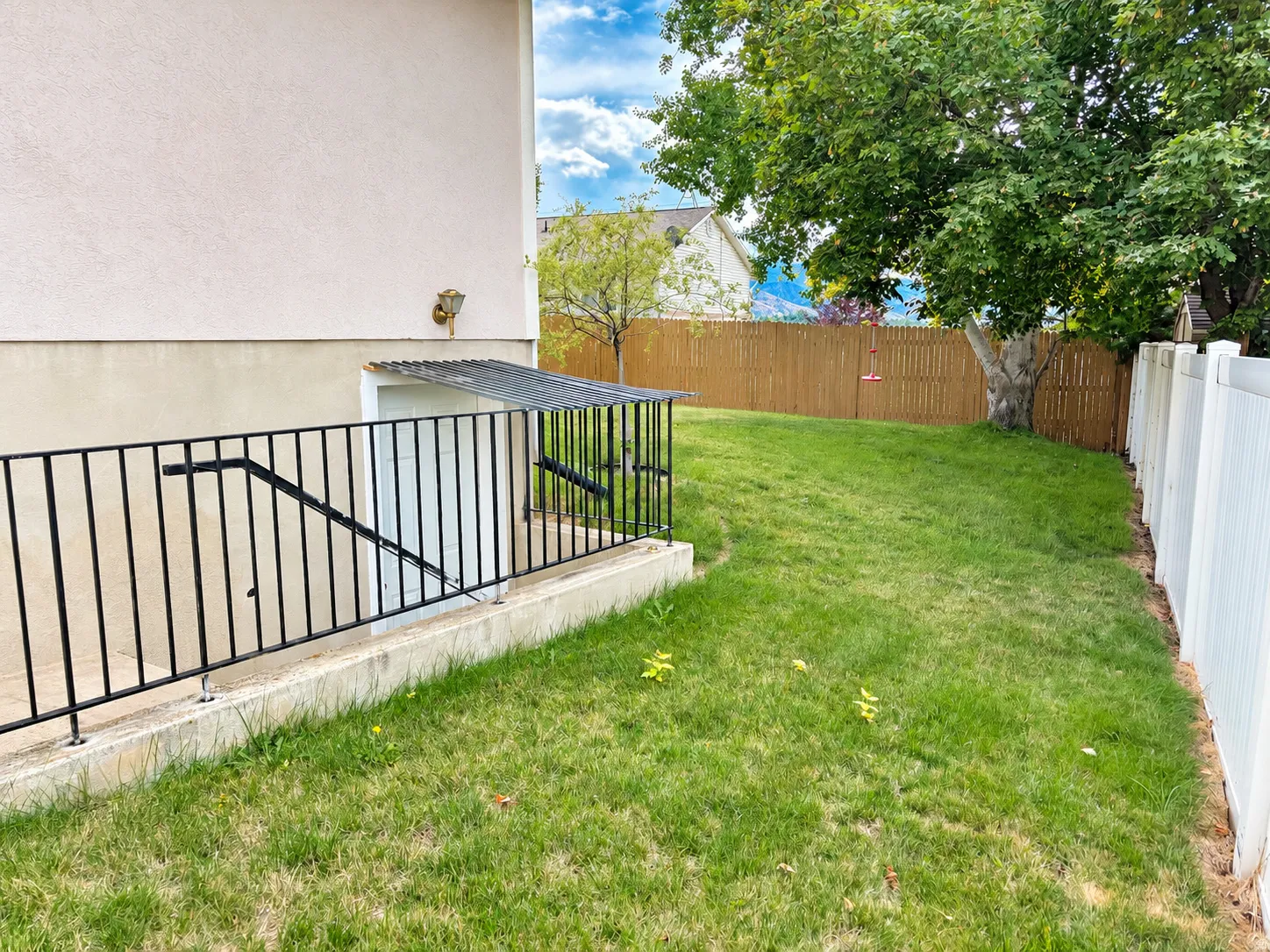 Expansive backyard featuring a manicured lawn, established shade tree, and wood privacy fencing
