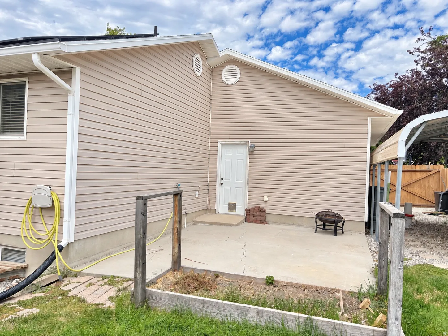 Exterior siding construction with a concrete patio, white door, and carport structure