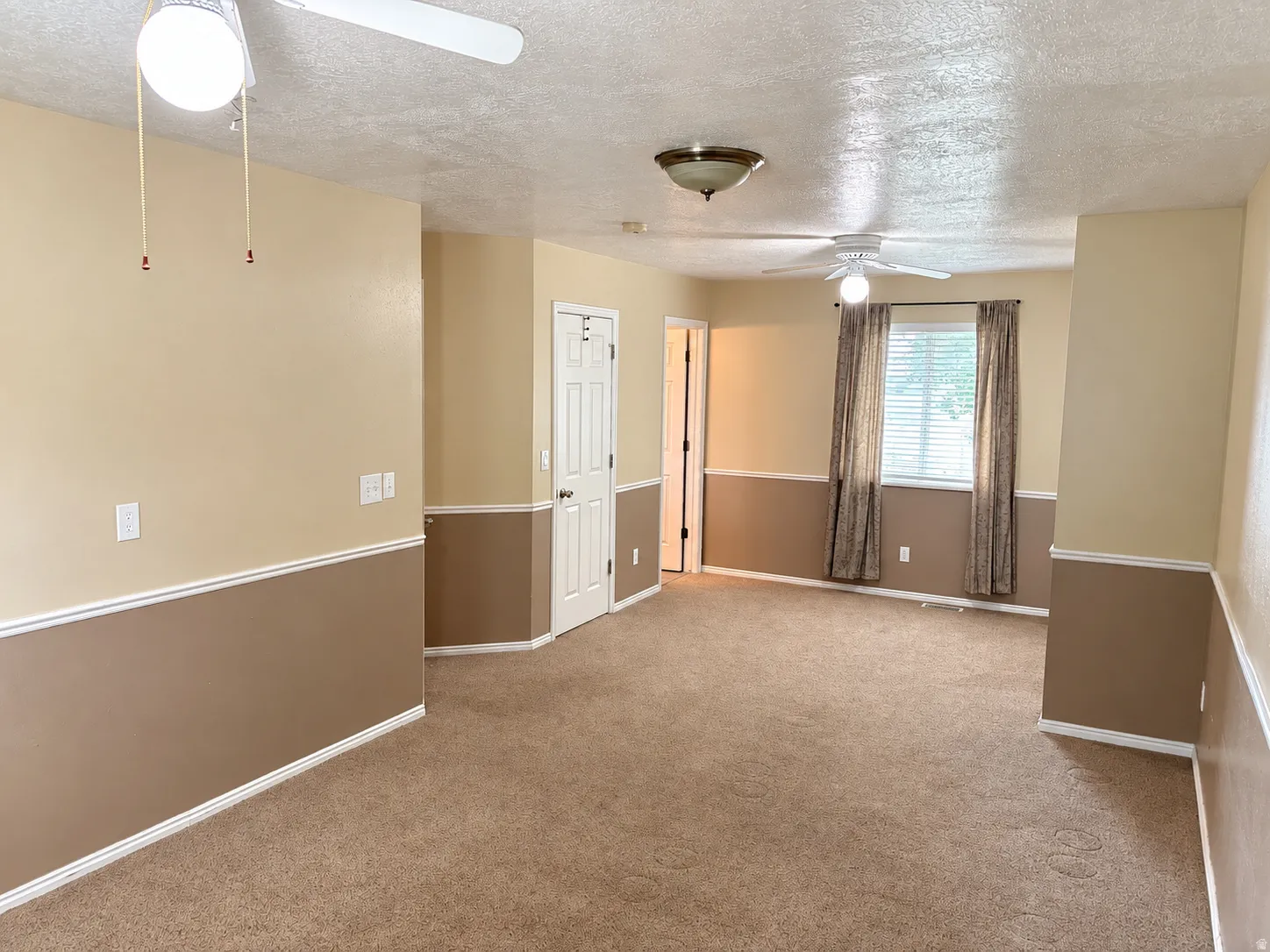 Spacious room featuring neutral carpeting, two-tone wall paint with white trim, and two ceiling fans for climate control