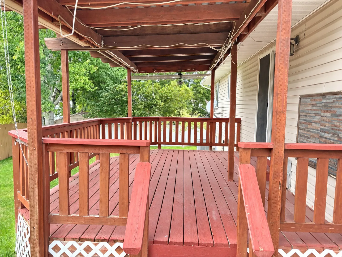 Expansive red-stained wood deck featuring a covered pergola, full balustrade, and lattice skirting