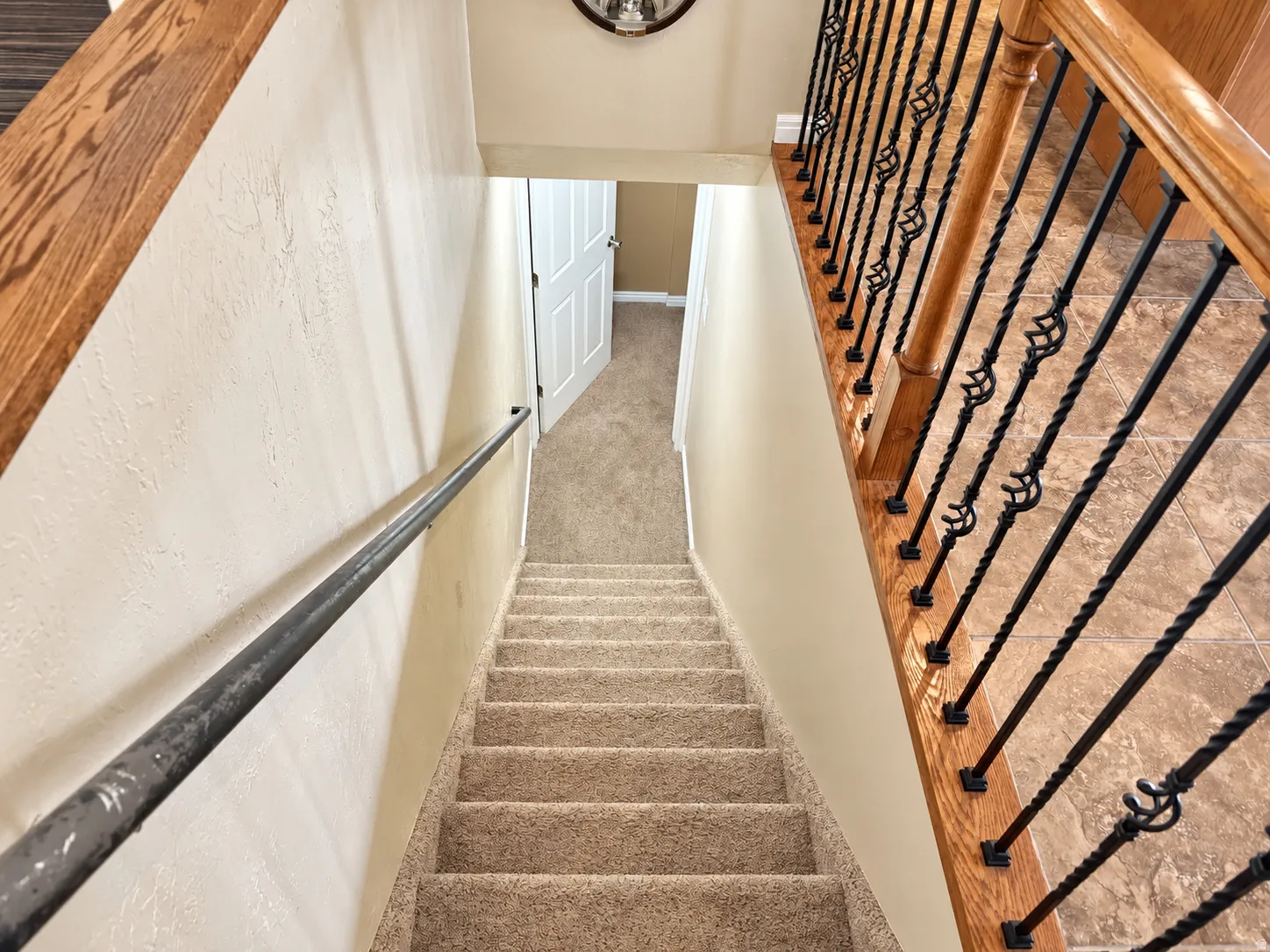 Staircase with carpeted treads, wood-finish handrails, and decorative black iron balusters