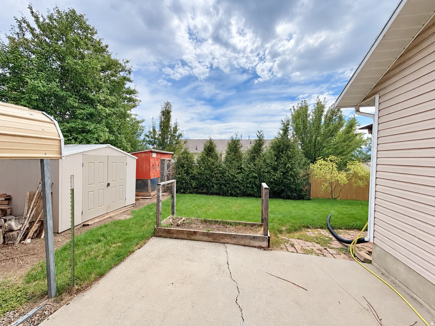 Expansive backyard featuring a concrete patio, a raised garden bed, a storage shed, and mature perimeter trees