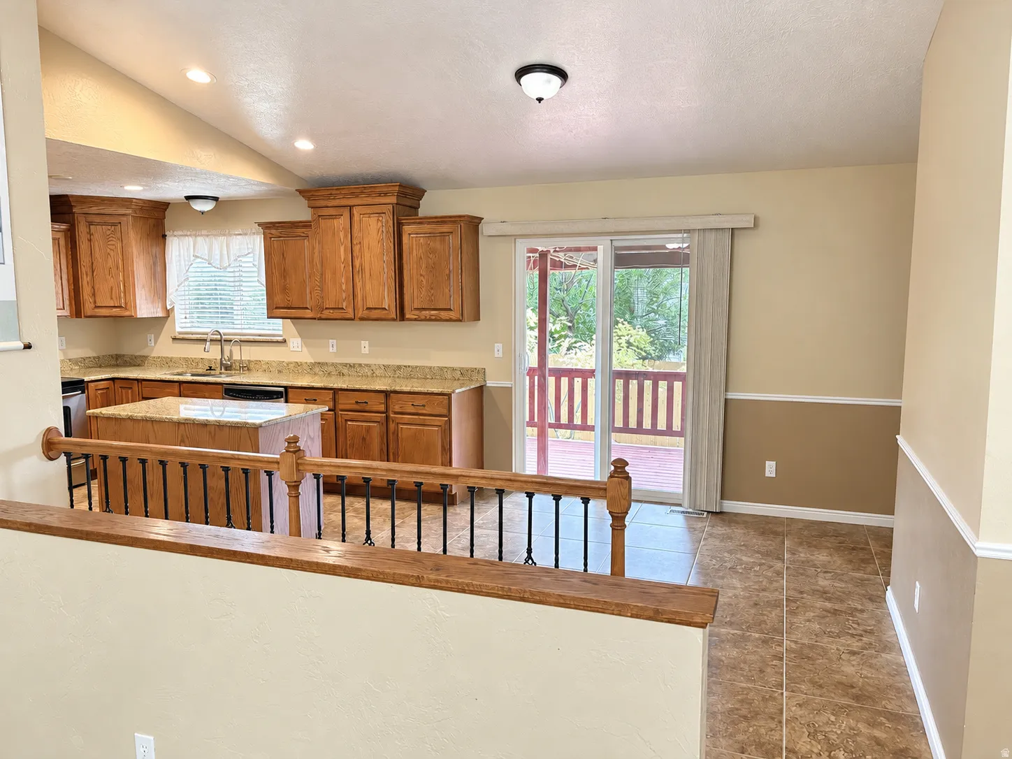 Vaulted ceiling, wood-finish cabinetry, central island with countertop, sliding glass door, and tiled flooring