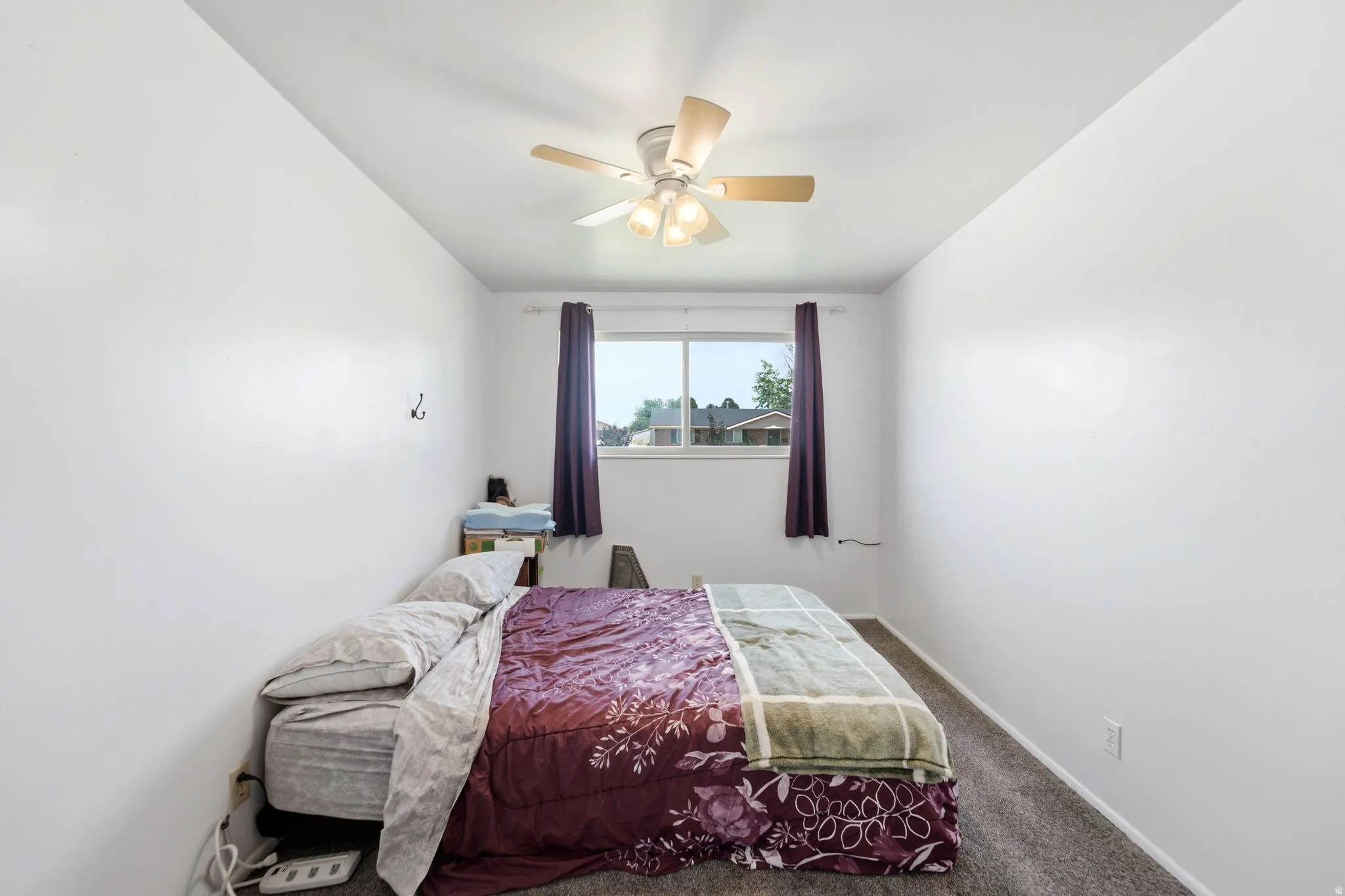 Room with white walls, a ceiling fan with light fixture, and a window featuring dark curtains