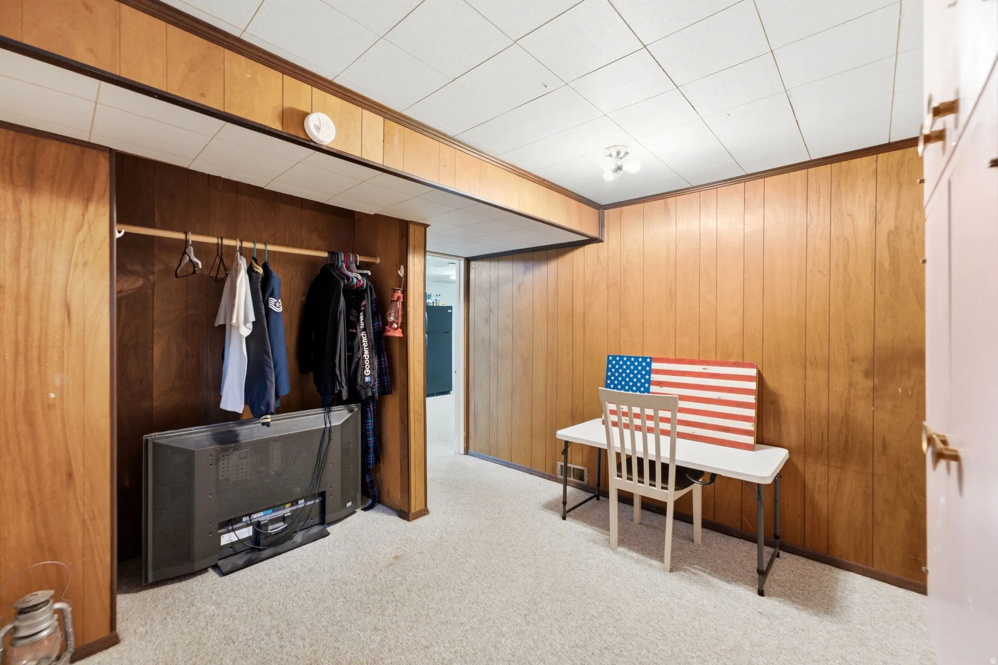 Room featuring wood paneling, acoustic tile ceiling, and neutral carpeting