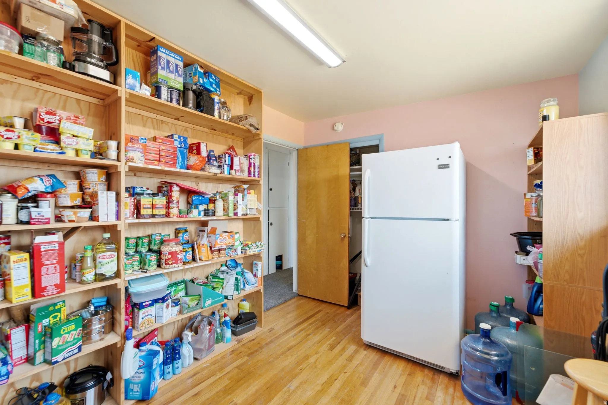 Storage room featuring extensive built-in wooden shelving, a white top-freezer refrigerator, and wood-finish flooring