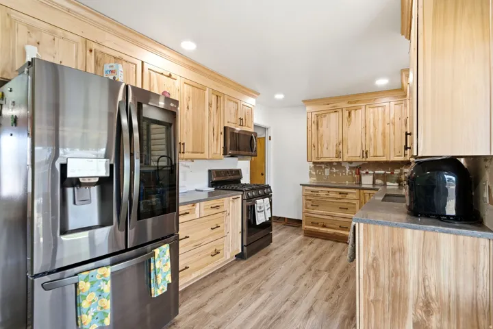 Kitchen featuring light wood cabinetry with dark hardware, stainless steel refrigerator, black range, and light-tone countertops