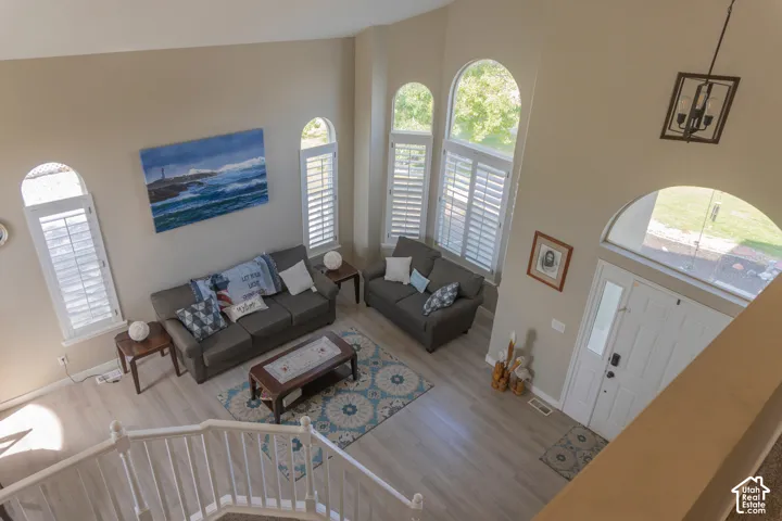Two-story living area featuring a vaulted ceiling, light wood-finish flooring, and multiple arched windows with plantation shutters