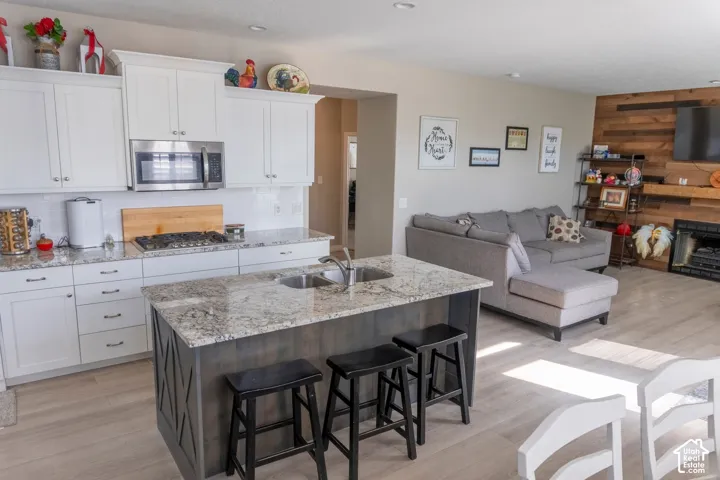 Open-concept living space with a kitchen island featuring a double-basin sink and bar seating, white shaker-style cabinetry, and stainless steel appliances
