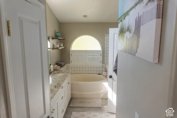 Soaking tub with white subway tile surround, arched window, and integrated privacy shutters