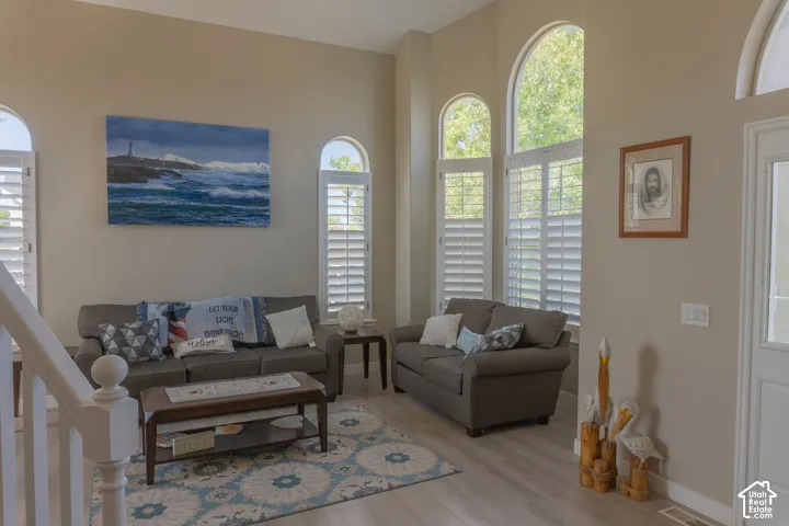 Vaulted ceiling family room featuring arched windows with plantation shutters, light wood-finish flooring, and a white staircase with a prominent newel post