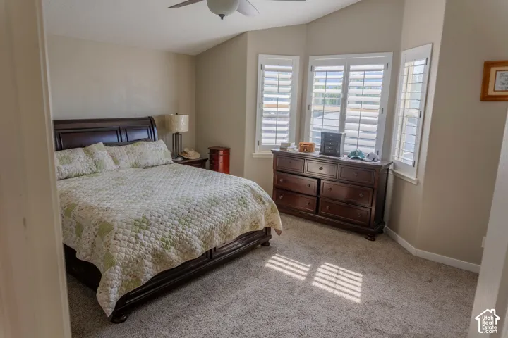 Carpeted room featuring a ceiling fan, bay windows with louvered shutters, and vaulted ceilings