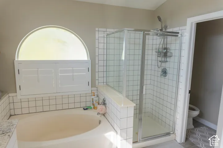 Tiled bathroom featuring a built-in soaking tub, arched window with plantation shutters, and a glass-enclosed shower with white subway tile