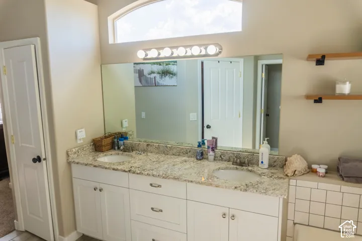 Bathroom vanity featuring dual undermount sinks with chrome fixtures, a stone-finish countertop, and white cabinetry