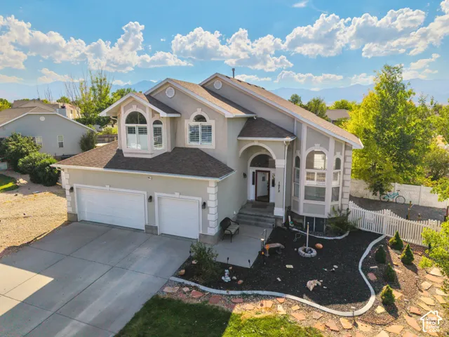 Two-story residence featuring light-toned stucco siding, decorative corner quoins, an arched entryway, a three-car garage, and mountain-range backdrop