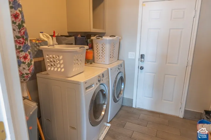 Dedicated laundry area featuring a front-load washer and dryer, upper cabinetry for storage, and wood-look tile flooring