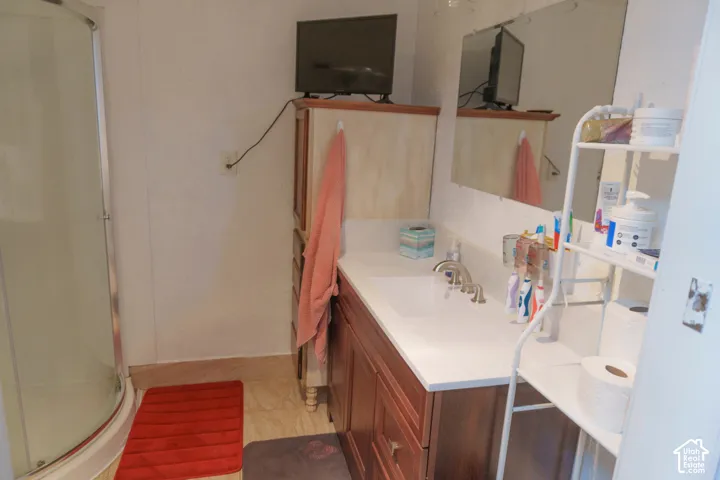 Bathroom featuring a curved glass shower enclosure, single vanity with integrated sink, wood-finish cabinetry, and a wall-mounted mirror