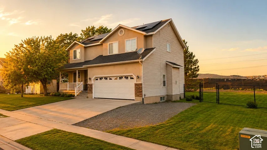 Contemporary residence featuring a two-car garage, covered front porch, a well-maintained lawn, solar panels, and a fenced backyard.