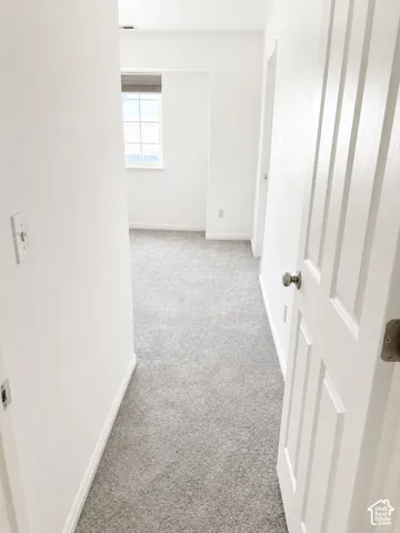 Hallway featuring light gray carpeting, white baseboards, and a paneled door with a brushed nickel knob