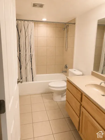 Bathroom featuring a tub/shower combination with beige tile surround, a light wood-finish vanity with an integrated basin sink, and neutral tile flooring