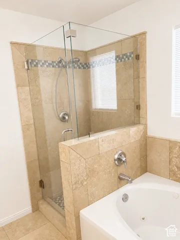 Travertine-tiled shower with a clear glass enclosure and a decorative mosaic border