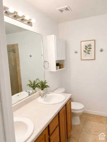 Bathroom featuring a dual-sink vanity with wood cabinetry and a light-toned countertop, a full-width mirror with vanity lighting, and tile flooring
