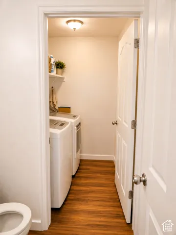 Dedicated laundry area featuring wood-finish flooring, white walls, overhead lighting, and an integrated shelf