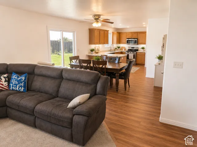 Open-concept living space featuring wood-finish flooring, a kitchen with stainless steel appliances, a ceiling fan with integrated lighting, a dining area, and sliding glass doors to the exterior