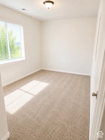 Bright room featuring neutral-toned carpet, white walls, and a window with horizontal blinds
