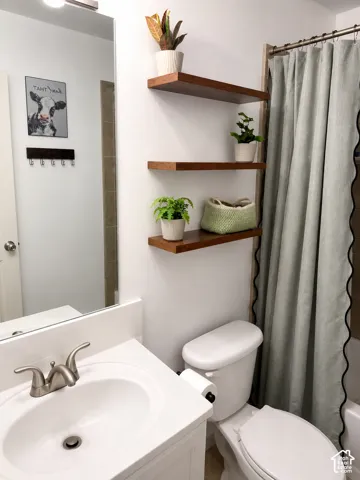 Bright bathroom featuring a white vanity with an integrated sink and brushed nickel faucet, a white toilet, and three wall-mounted wood-finish floating shelves