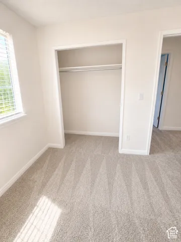 Bedroom featuring light-colored carpet flooring, a window with blinds, and a built-in closet with a hanging rod