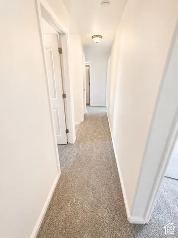 Hallway with light gray carpet flooring, white walls, and white trim
