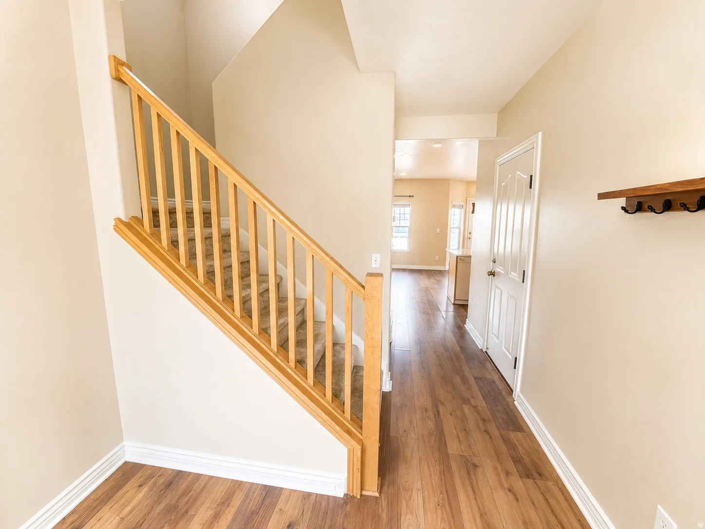 Entryway featuring wood-finish flooring, light tan wall paint, white trim, and a carpeted staircase with wood banister