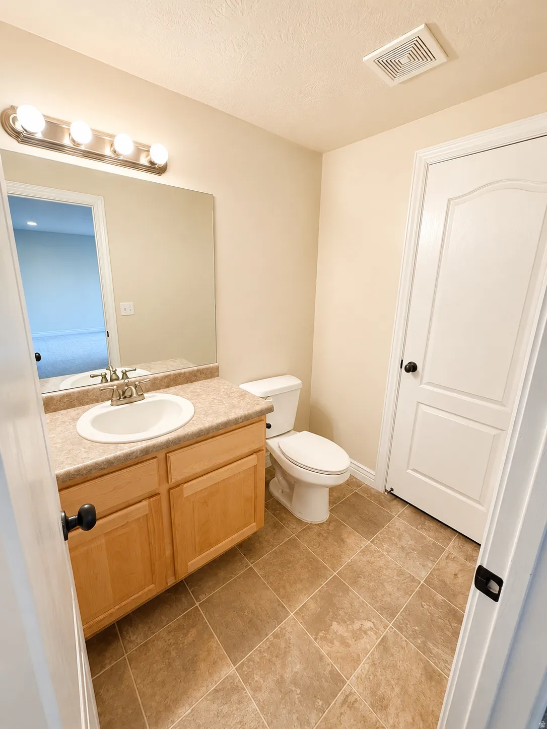 Bathroom featuring a wood-finish vanity with a laminate countertop, an undermount sink, and a vanity mirror with overhead lighting