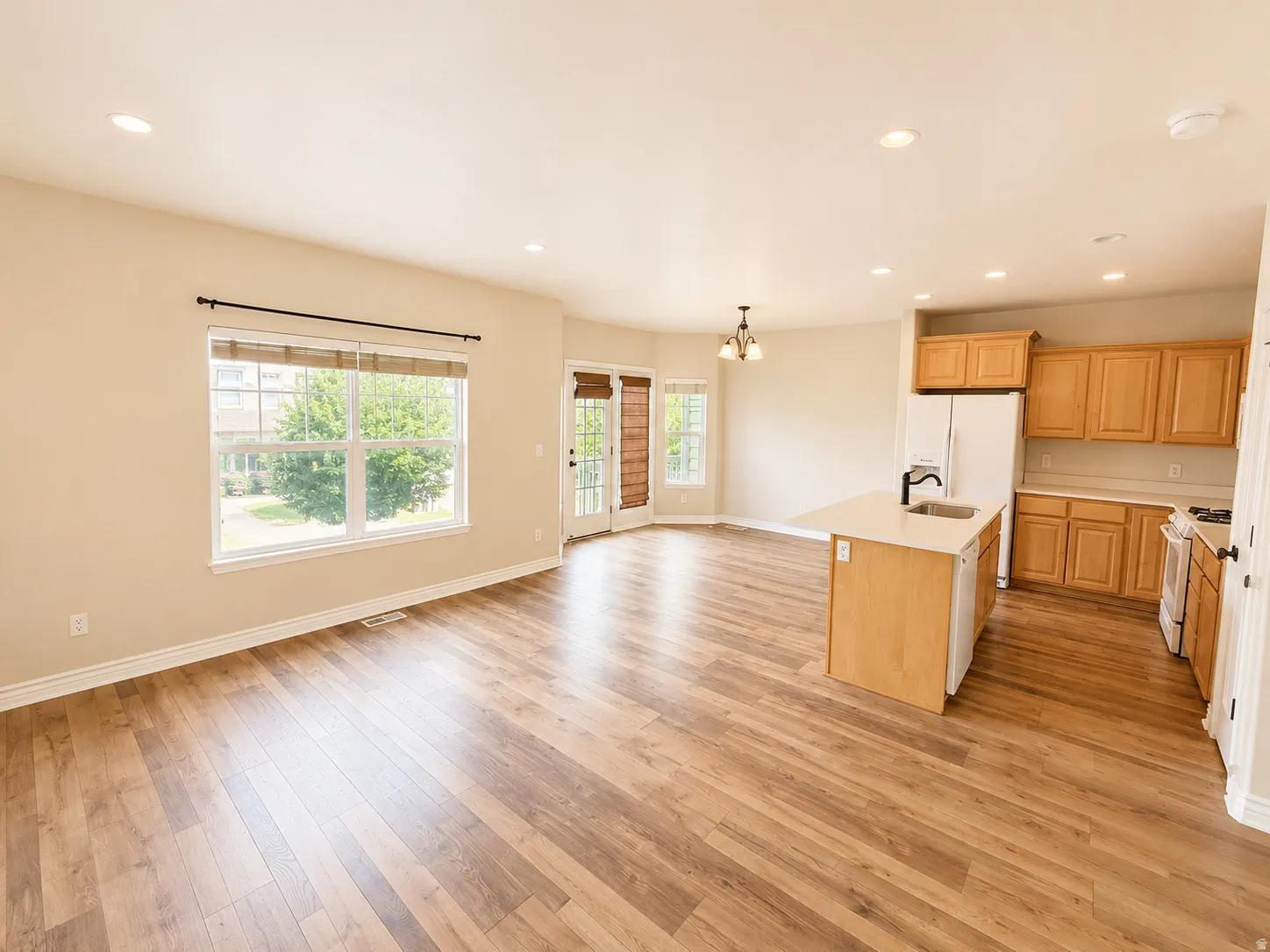 Expansive open-concept living area featuring wood-finish flooring, recessed lighting, and a kitchen island with an integrated sink