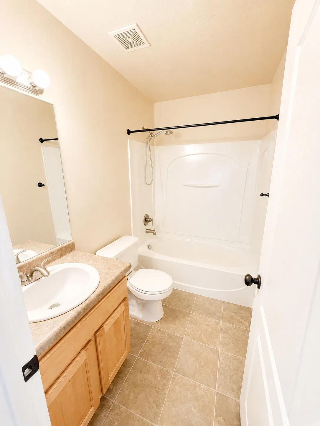 Bathroom featuring a light wood-finish vanity with an integrated sink, a full bathtub with a shower, and neutral-toned square tile flooring