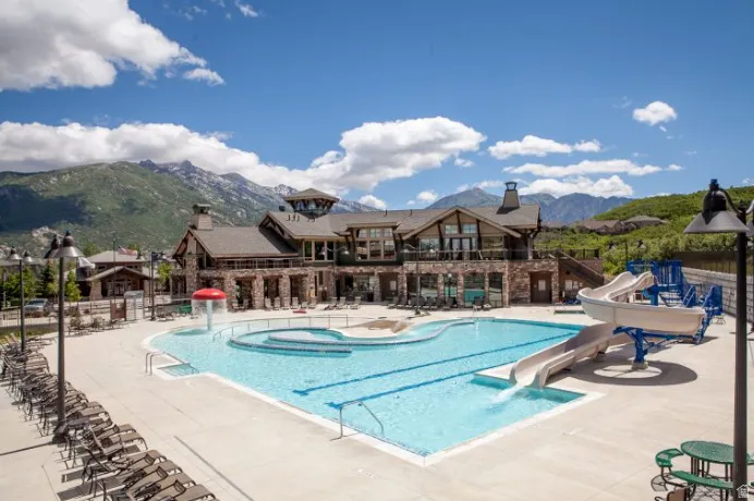 Community swimming pool with water slides and a built-in spa, framed by a stone and wood-clad clubhouse featuring an elevated balcony